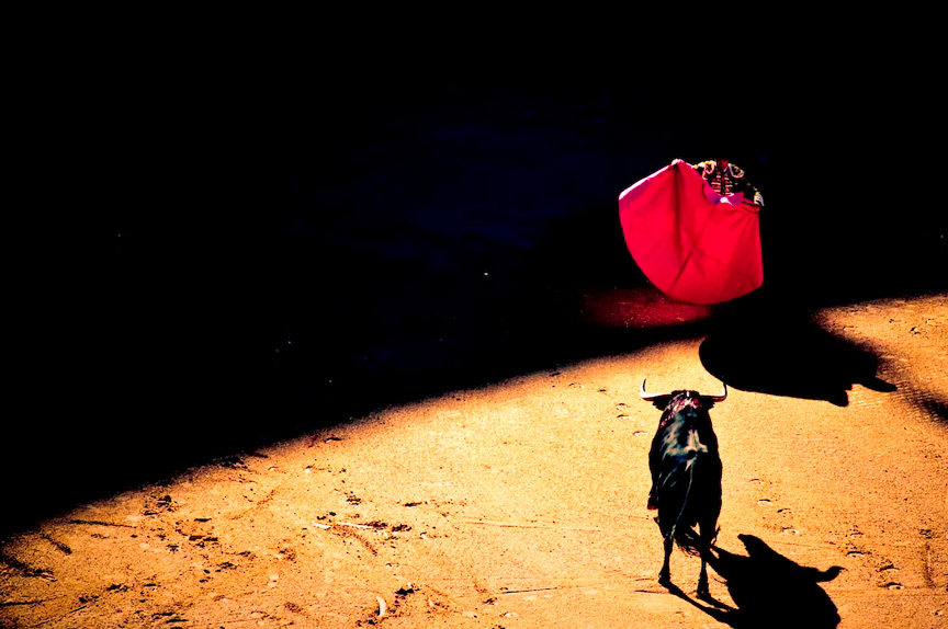 A matador with a red cape facing off against an angry bull